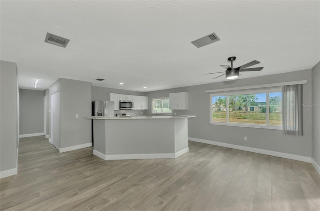 unfurnished living room with a textured ceiling, light wood-type flooring, and ceiling fan