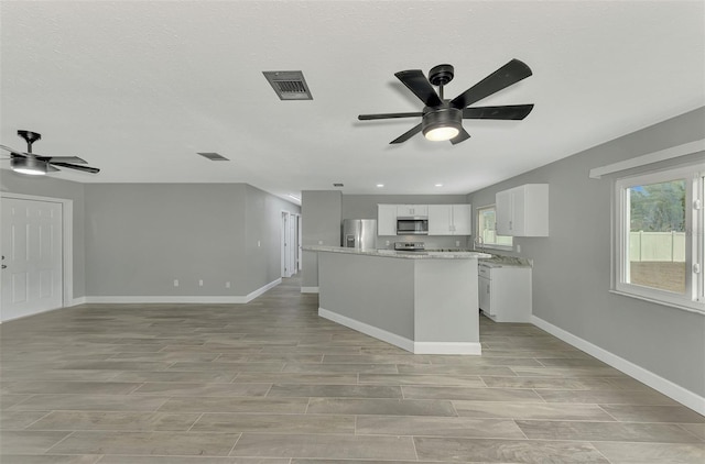 kitchen featuring ceiling fan, a center island, light stone countertops, white cabinets, and appliances with stainless steel finishes