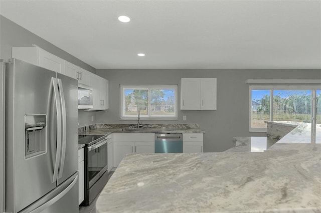 kitchen with stainless steel appliances, white cabinetry, and light stone counters