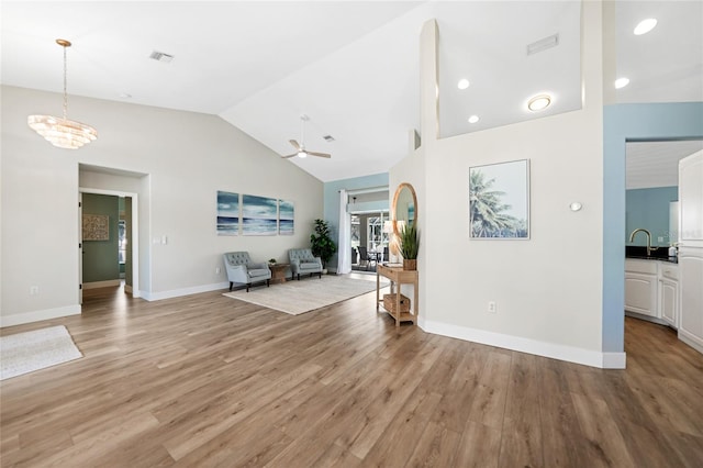 unfurnished living room featuring ceiling fan with notable chandelier, light wood-type flooring, sink, and vaulted ceiling