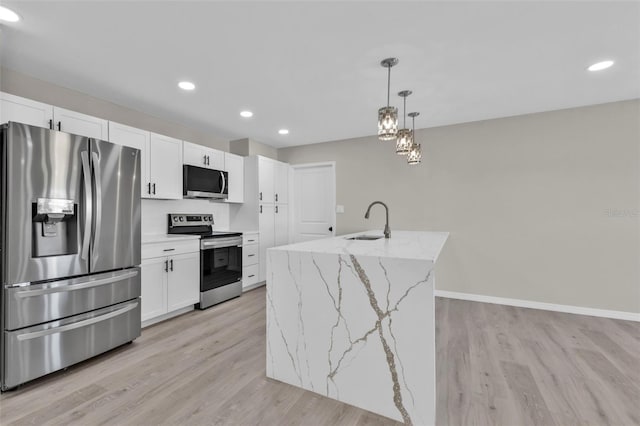 kitchen with light stone countertops, stainless steel appliances, sink, decorative light fixtures, and an island with sink