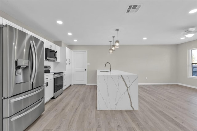 kitchen with appliances with stainless steel finishes, sink, pendant lighting, white cabinets, and light hardwood / wood-style floors