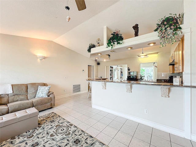 kitchen with kitchen peninsula, a kitchen breakfast bar, decorative backsplash, lofted ceiling, and light tile patterned flooring