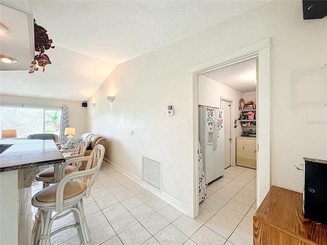 dining area featuring washer / dryer, light tile patterned floors, and vaulted ceiling