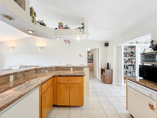 kitchen with kitchen peninsula, white dishwasher, vaulted ceiling, stone countertops, and light tile patterned flooring