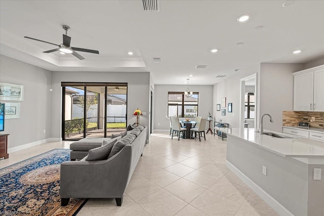 living room with light tile patterned floors, ceiling fan with notable chandelier, crown molding, and sink