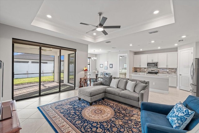 tiled living room with ceiling fan with notable chandelier, a raised ceiling, and crown molding