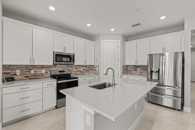 kitchen with appliances with stainless steel finishes, light stone counters, sink, white cabinetry, and an island with sink