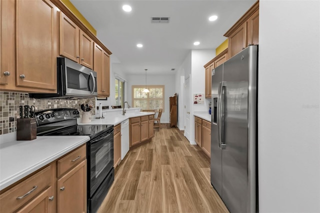 kitchen with appliances with stainless steel finishes, backsplash, sink, light hardwood / wood-style floors, and hanging light fixtures