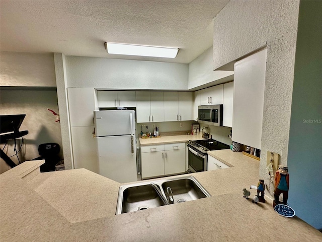 kitchen with sink, kitchen peninsula, a textured ceiling, white cabinets, and appliances with stainless steel finishes