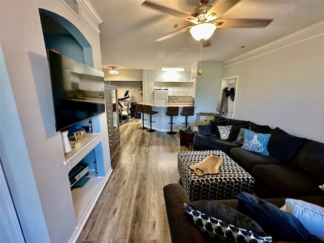 living room featuring a ceiling fan, visible vents, crown molding, and light wood finished floors