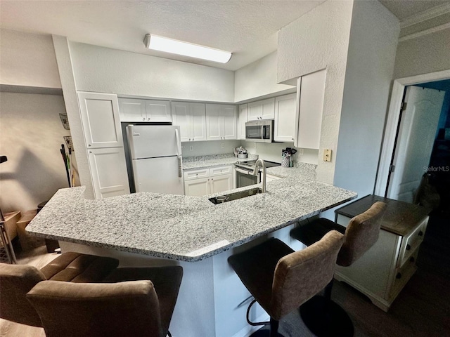 kitchen featuring appliances with stainless steel finishes, a sink, light stone countertops, a peninsula, and a kitchen breakfast bar