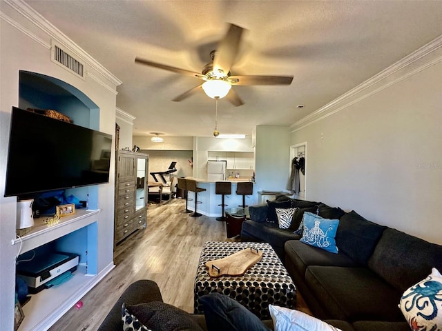 living room with ornamental molding, light wood-type flooring, visible vents, and ceiling fan