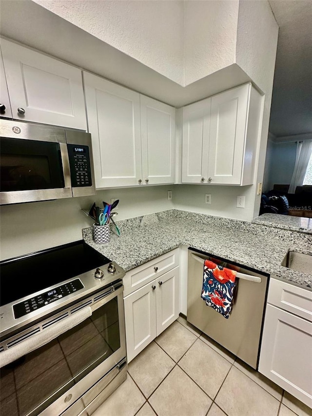 kitchen featuring stainless steel appliances, light tile patterned flooring, and white cabinets