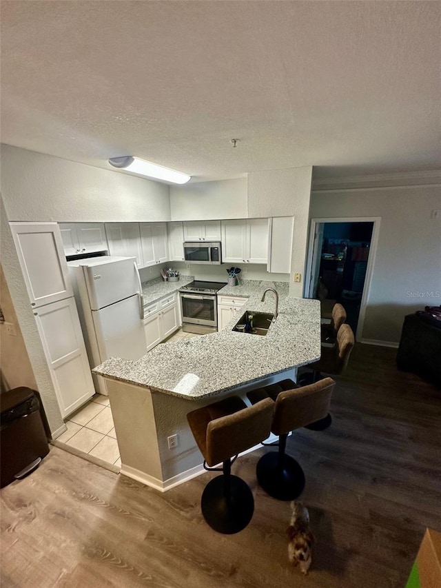 kitchen with a breakfast bar, stainless steel appliances, a sink, light stone countertops, and a peninsula