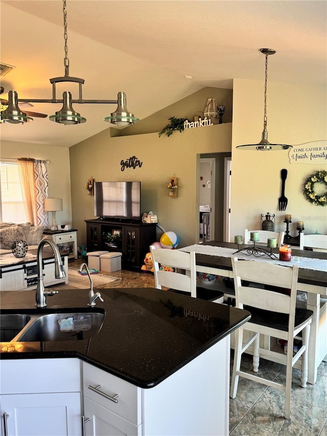 kitchen with pendant lighting, lofted ceiling, dark stone counters, sink, and white cabinetry