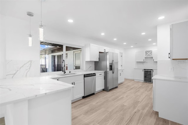 kitchen featuring stainless steel appliances, beverage cooler, sink, white cabinetry, and hanging light fixtures