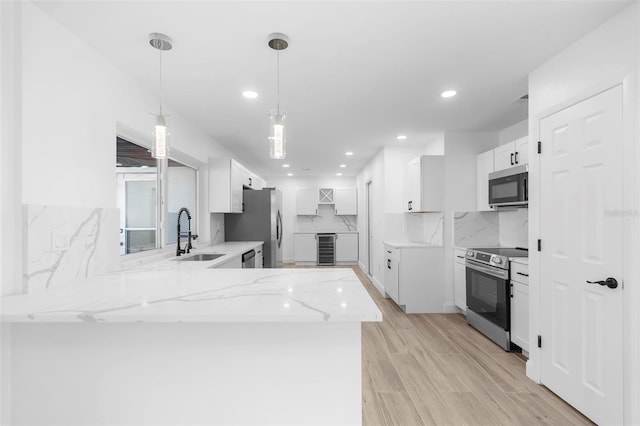 kitchen with kitchen peninsula, appliances with stainless steel finishes, white cabinetry, and sink