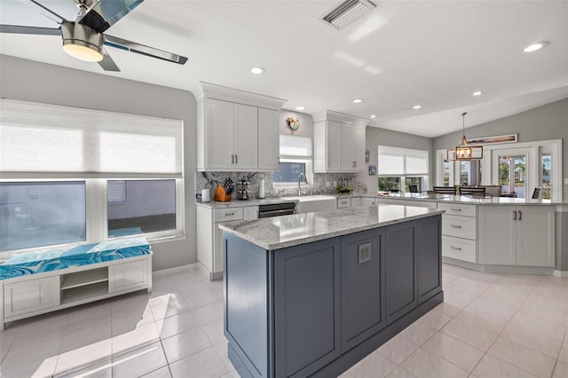 kitchen featuring light stone counters, vaulted ceiling, a kitchen island, white cabinetry, and hanging light fixtures