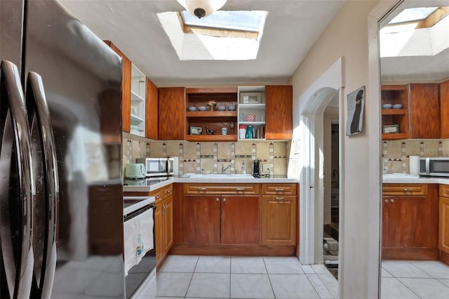 kitchen featuring stainless steel appliances, light tile patterned floors, decorative backsplash, and a skylight