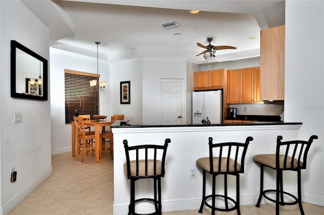 kitchen featuring white fridge with ice dispenser, hanging light fixtures, kitchen peninsula, a breakfast bar, and ceiling fan with notable chandelier