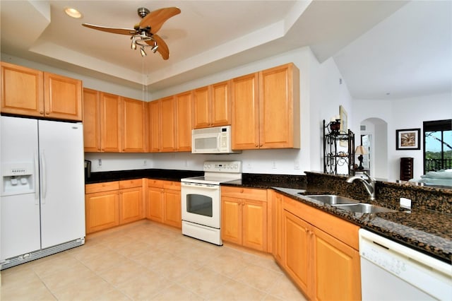 kitchen with dark stone counters, white appliances, a tray ceiling, ceiling fan, and sink