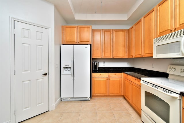 kitchen featuring a raised ceiling, dark stone countertops, light tile patterned flooring, and white appliances