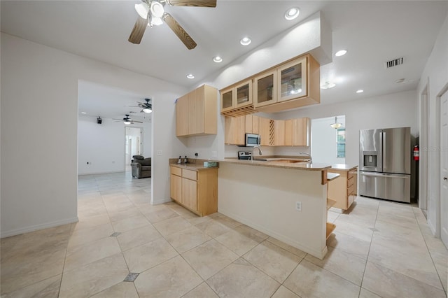 kitchen featuring light brown cabinetry, a breakfast bar area, light tile patterned floors, kitchen peninsula, and stainless steel appliances