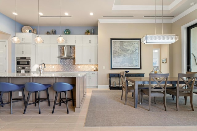 kitchen featuring white cabinets, hanging light fixtures, wall chimney exhaust hood, decorative backsplash, and light stone countertops