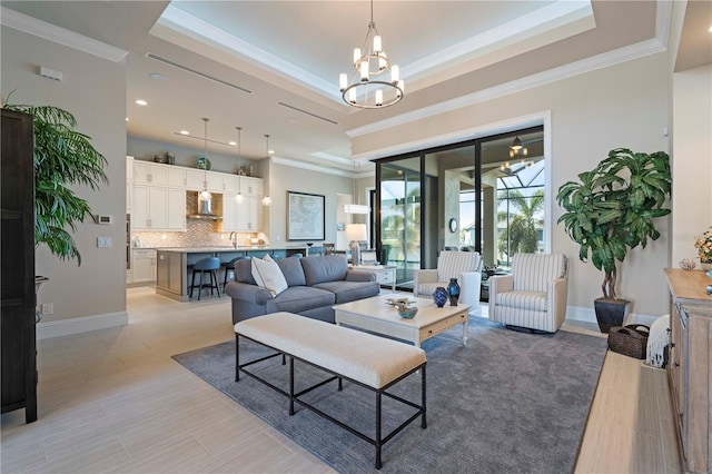 living room featuring a raised ceiling, ornamental molding, sink, and an inviting chandelier