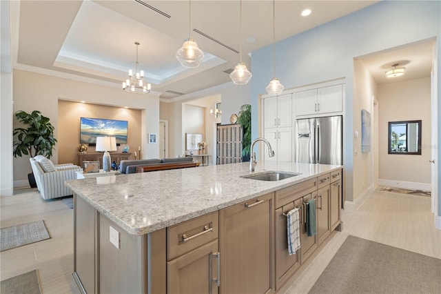 kitchen with light stone countertops, sink, a raised ceiling, pendant lighting, and a kitchen island with sink