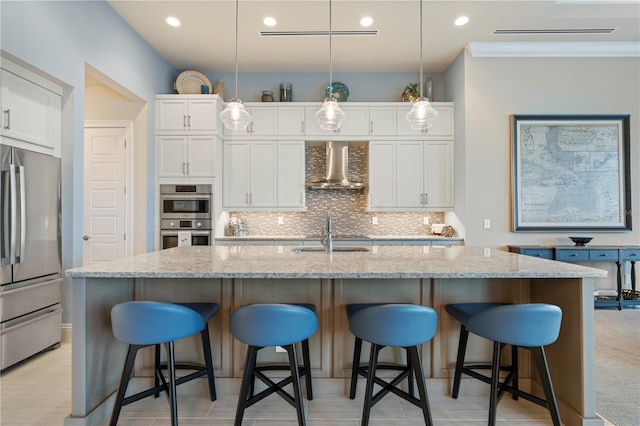 kitchen with a kitchen island with sink, white cabinets, stainless steel appliances, and wall chimney range hood