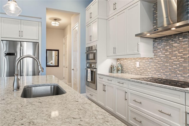 kitchen with wall chimney exhaust hood, stainless steel appliances, sink, white cabinets, and hanging light fixtures