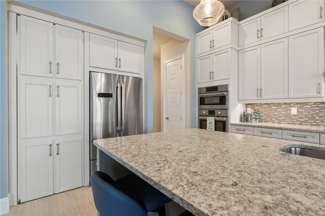 kitchen with white cabinets, backsplash, stainless steel appliances, and light stone countertops