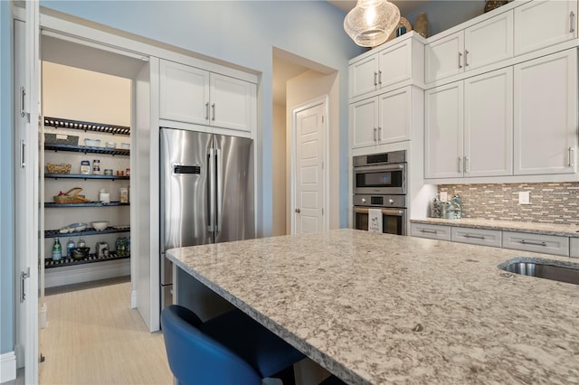 kitchen with white cabinetry, decorative backsplash, light stone countertops, and stainless steel appliances