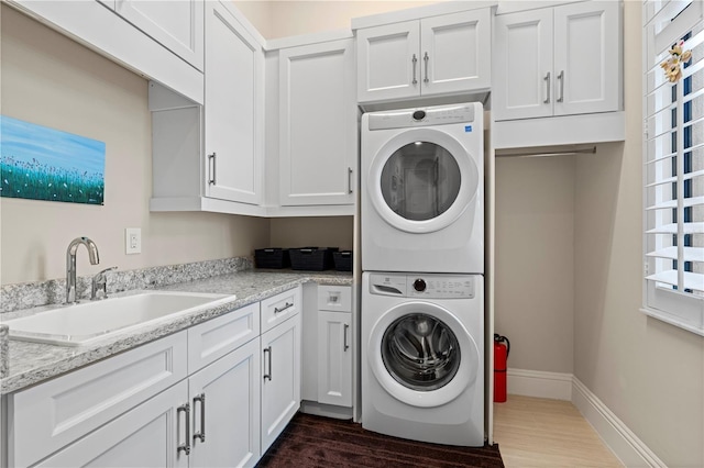 laundry area featuring stacked washer and dryer, cabinets, dark hardwood / wood-style floors, and sink