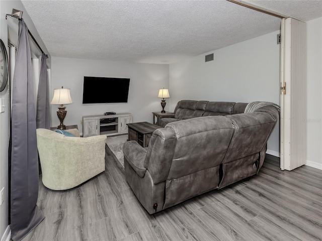 living area featuring light wood finished floors, baseboards, visible vents, and a textured ceiling