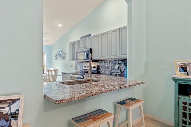 kitchen with tasteful backsplash, light stone countertops, a breakfast bar area, and appliances with stainless steel finishes