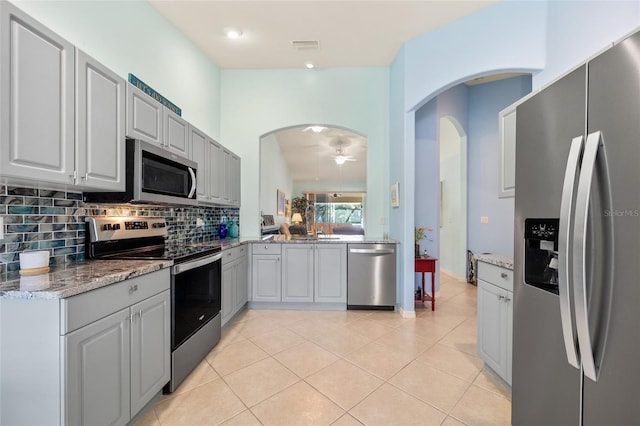 kitchen with gray cabinetry, backsplash, light stone countertops, light tile patterned floors, and stainless steel appliances