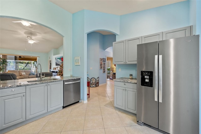 kitchen featuring light stone counters, stainless steel appliances, ceiling fan, sink, and gray cabinets