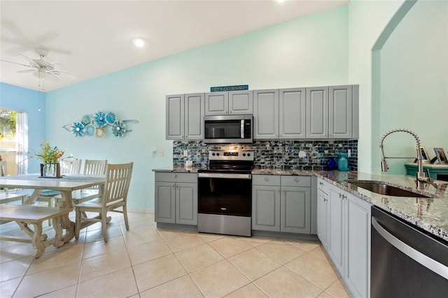 kitchen with sink, light stone counters, gray cabinets, decorative backsplash, and appliances with stainless steel finishes