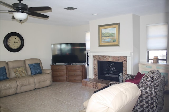 tiled living room featuring a stone fireplace and ceiling fan