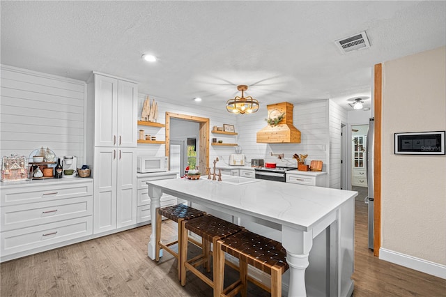 kitchen featuring light stone countertops, decorative light fixtures, a breakfast bar area, a center island with sink, and white cabinets