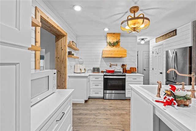 kitchen featuring stainless steel appliances, ventilation hood, pendant lighting, white cabinets, and wood walls