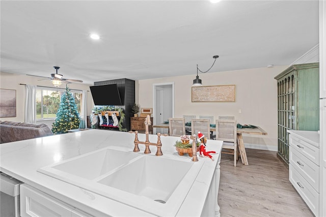 kitchen with pendant lighting, sink, ceiling fan, light wood-type flooring, and white cabinetry