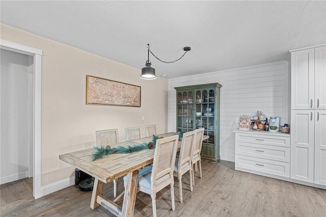 dining space featuring a textured ceiling, wooden walls, and light hardwood / wood-style flooring