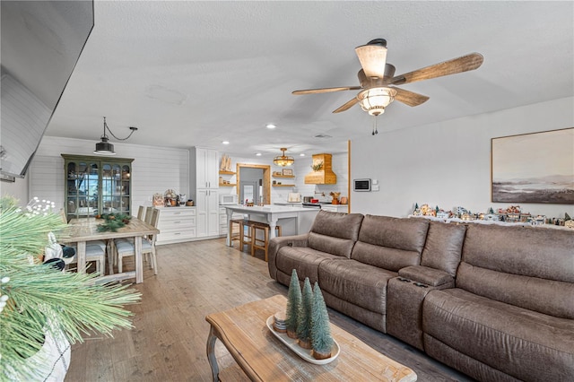 living room featuring ceiling fan, light wood-type flooring, and a textured ceiling