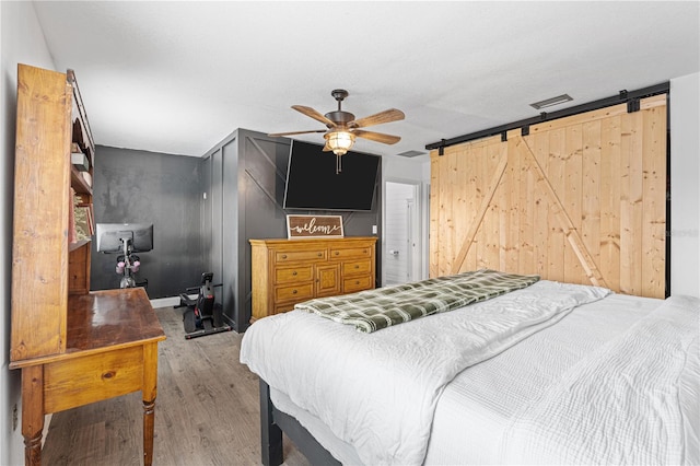 bedroom featuring a barn door, ceiling fan, and light wood-type flooring