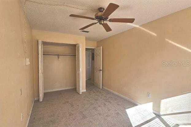 unfurnished bedroom with ceiling fan, light carpet, a textured ceiling, and a closet