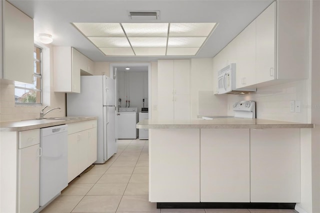 kitchen featuring kitchen peninsula, white appliances, washer and dryer, white cabinets, and light tile patterned flooring